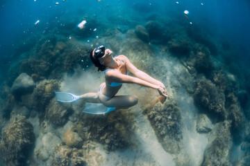 Fototapeta na wymiar Woman glides with sand in hand. Free diver with fins posing underwater