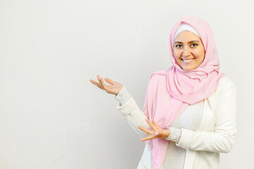 Young pretty Muslim Arab woman in pink hijab standing isolated over the gray background and presenting pointing with hands on the blank space for advertisement, mockup image for health care concept,