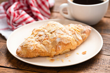 Almond croissant on a plate served with a cup of black coffee on wooden table. Closeup view