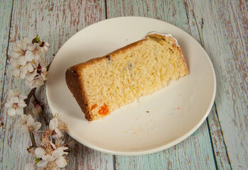 Easter composition. A branch of a blooming apricot and a piece of glazed Easter cake close-up on a white plate on a light wooden background. Happy Easter Holidays. Selective focus.