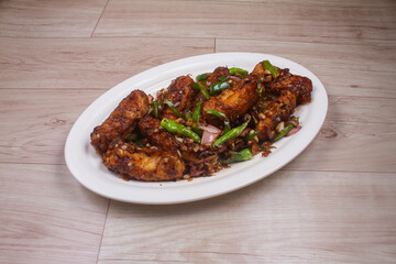 Paneer Chilis is an Indian dish, paneer cubes with tomatoes, onions, spring onions, chilli sauce. served on rustic wooden background, selective focus