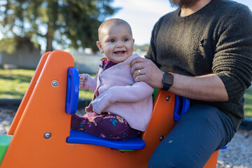 Adorable happy baby and her father on colorful seesaw
