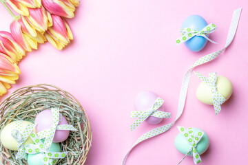 Basket easter decoration: Colourful egg with tape ribbon, spring tulips, white feathers on pastel pink background. Congratulatory easter design. Top view.