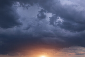 Naklejka na ściany i meble Dark storm cumulus clouds with yellow orange sun and sunlight on sunset, sunrise