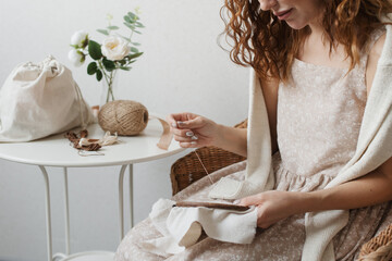 A woman in a beige dress embroiders with threads on a linen fabric