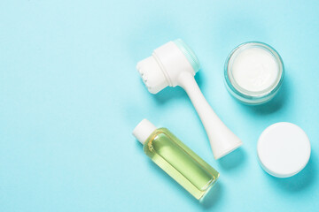 Beauty product. Face massage brush, cream for face and gel on blue background. Skin care concept. Flat lay image with copy space.
