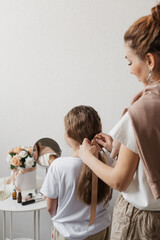 Mom collects her daughter's hair in a beautiful ponytail and ties her hair with a ribbon