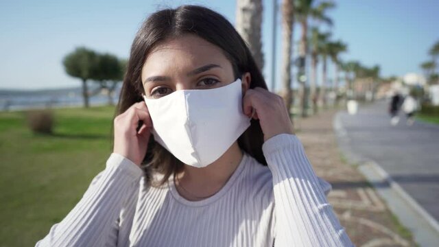 End of Coronavirus pandemic and back to normality concept. Close up of confident girl outdoor in a park of an ocean sea town wearing the protective mask looking at camera then takes off it and smiling