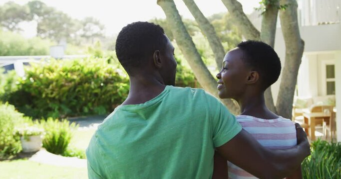 Rear view of smiling african american couple embracing in sunny garden