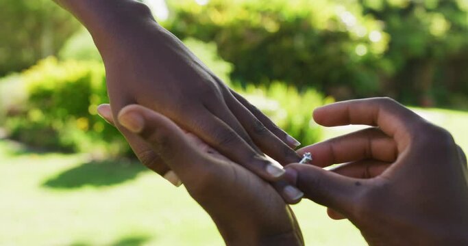 African american couple in sunny garden man proposing putting ring on her finger