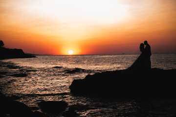 Wedding couple, groom, bride with bouquet posing near sea and blue sky