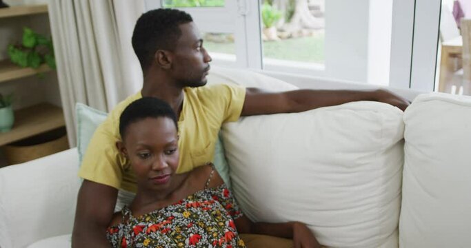 African american couple reclining on sofa embracing looking out of window and at each other