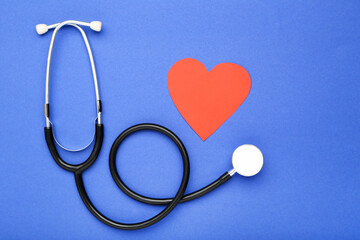 Stethoscope with red paper heart on blue background
