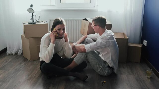 Happy couple relaxes after moving in a new home. Couple sits on floor and woman talks on phone
