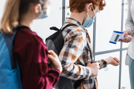 Teacher checking temperature of pupil with infrared thermometer during quarantine