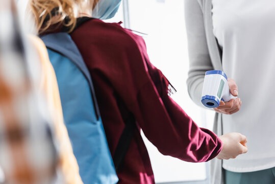 Cropped view of teacher checking temperature of pupil in medical mask with infrared thermometer - Powered by Adobe