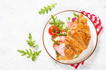 Croissant sandwich with ham, cheese and fresh salad in white plate. Top view with copy space on white stone table.