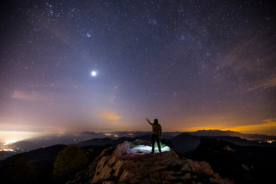 Rear view of a man standing on a mountain at night pointing to sky, Mare De Deu Del Mont, La Garrotxa, Girona, Catalonia, Spain