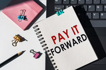 Notebook with tools and notes about PAY IT FORWARD lies on laptop.