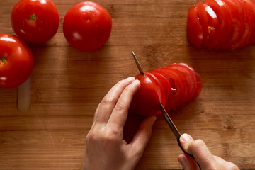 Woman cutting tomato on wooden board, close-up. Woman hands with knife chopping tomatoes