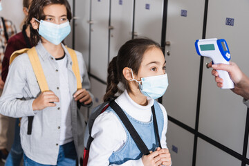 Fototapeta na wymiar Schoolkid in medical mask standing near teacher measuring temperature in school corridor