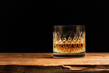 Vaso de whiskey sobre una mesa de madera rústica y un fondo negro. Vista de frente y de cerca....