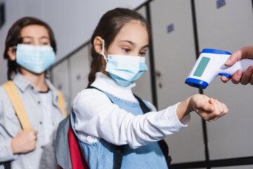 Fototapeta na wymiar Teacher with non contact thermometer measuring temperature of schoolgirl in medical mask