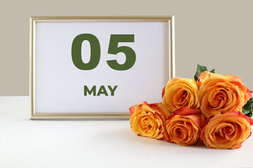 day of the month 05 May calendar photo frame and yellow rose on a white table