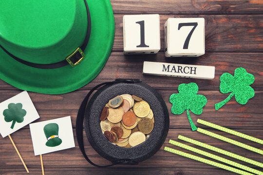 Pot of coins with cube calendar, flags with pictures, straws and clover leafs on brown wooden background