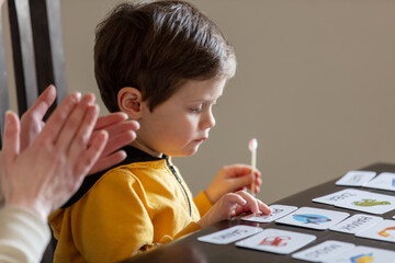 little boy learns words from cards under the ABA therapy program at home at the table