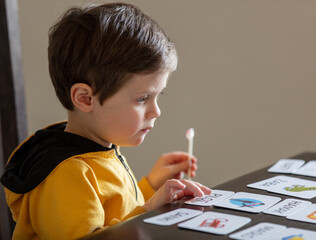 little boy learns words from cards under the ABA therapy program at home at the table