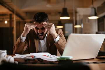 Young businessman working with laptop at office. Tired man sitting at office desk working on laptop computer