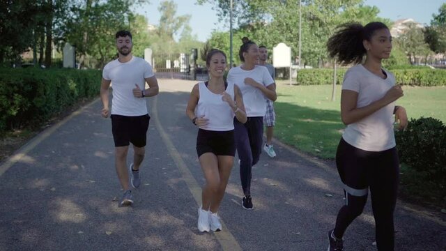 Get in shape after the winter by going for a run in the city park with friends. Group of young multiracial happy people training outdoor jogging together in the green