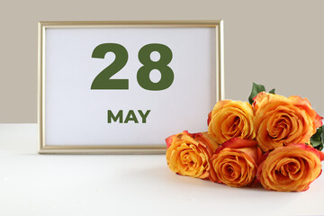 day of the month 28 May calendar photo frame and yellow rose on a white table