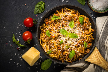 Pasta Bolognese, meat ragout in tomato sauce in the skillet at black table. Top view with copy space.
