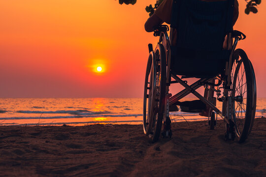 Asian Special Child On Wheelchair On The Sea Beach With Sunset On Travel Time In Holiday Family And Learning About Nature Around The Sea,Lifestyle In The Education Age Kids,Happy Disabled Kid Concept.