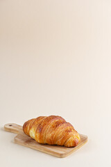 Croissant on a wooden board on a beige background.
