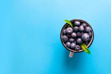 Top view of fresh ripe blueberry berries with mint in a metal mug on a blue surface, flat lay, vertical photo