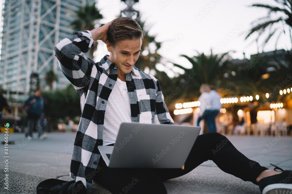 Poster pensive millennial male student checking mail and reading information from web page using laptop com