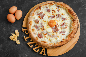 Homemade carbonara pizza with cream sauce, bacon, mozzarella parmesan and egg on a dark background. Top view, side view