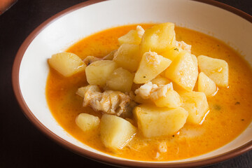 A plate of boiled potatoes with cod in a vegetable sauce on a dark wooden table. Fish and food.
