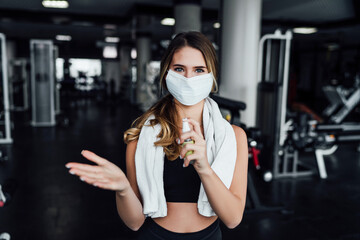 Safe sport, beautiful girl in the gym in a protective mask on her face and with an antiseptic