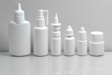 Monochrome grey color photo. A set of medical plastic white bottles, demonstrating a variety of medicinal forms, on a gray background.