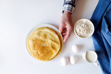 A lot of pancakes are stacked on a white plate. Thin pancakes with a crispy crust. Pancake day.