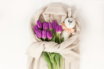 A bouquet of tulips and a knitted bunny on the background of a cream knitted sweater, a top view of a bouquet of tulips for women's day, the concept of spring flowers