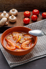 Tom yam soup with shrimps in a tureen on a concrete background next to a bowl with coconut milk tomatoes and mushrooms