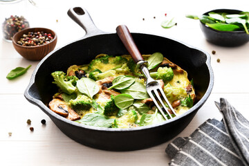 Omelet with spinach and mushrooms in a cast-iron pan on a light wood background. Fritata with spinach.