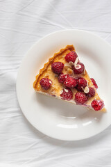 Piece of classic cheesecake with raspberry berries on a white plate on the bed.