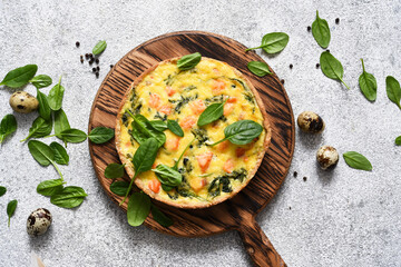Quiche with salmon and spinach, cheese on a light concrete background. View from above.