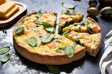 Tart with salmon and spinach, cheese on a black concrete background. Quiche with fish.